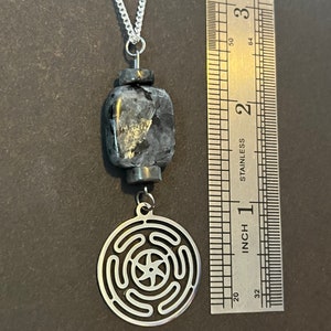 Puede incluir: Un collar de cadena de plata con un colgante de piedra negra y gris y un colgante de plata con un dise&ntilde;o circular. El collar se mide con una regla.