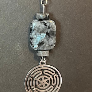 Puede incluir: Un collar de cadena de plata con un colgante de piedra gris oscuro y azul y un dije de plata con un dise&ntilde;o circular.