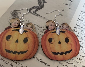 May include: A pair of Halloween-themed earrings. Each earring features a smiling orange pumpkin with a vintage illustration of children peeking over the top. The earrings have silver-colored hooks.