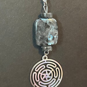 Puede incluir: Un collar de cadena de plata con un colgante de piedra azul oscuro y gris y un colgante circular de plata con un dise&ntilde;o de nudo celta.