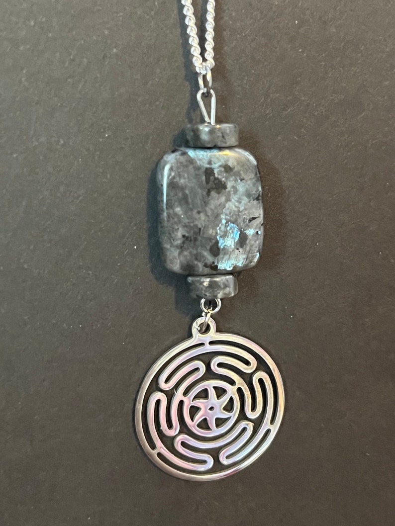Puede incluir: Un collar de cadena de plata con un colgante de piedra azul oscuro y gris y un colgante circular de plata con un dise&ntilde;o de nudo celta.