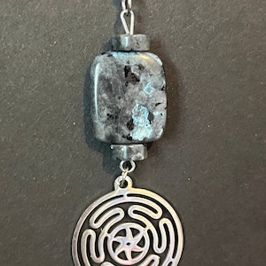 Puede incluir: Un collar de cadena de plata con un colgante de piedra azul oscuro y negro y un dije de plata con un dise&ntilde;o de laberinto circular.