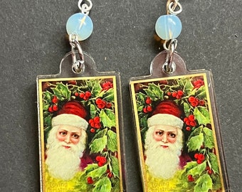 May include: A pair of silver earrings with a clear plastic charm featuring a vintage image of Santa Claus with the text "Loving Christmas Wishes". Each charm is topped with a white opal bead.