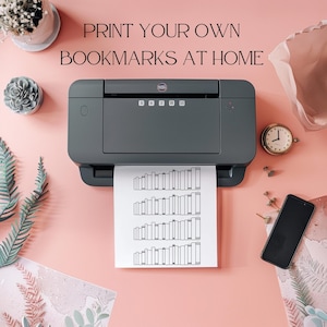 May include: A black and white printable bookmark design with a stack of books on a sheet of paper coming out of a black printer on a pink surface. The text "PRINT YOUR OWN BOOKMARKS AT HOME" is above the printer.
