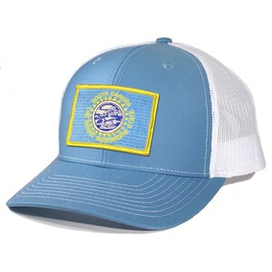 May include: A light blue trucker hat with a white mesh back. The hat features a patch of the South Dakota state flag on the front.