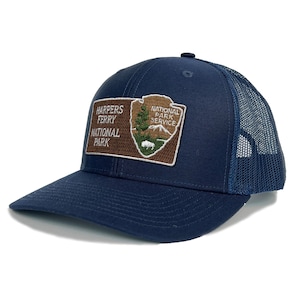 May include: Navy blue trucker hat featuring a patch with the text "HARPERS FERRY NATIONAL PARK" and the National Park Service logo. The hat has a mesh back and a curved brim. A stylish accessory for outdoor enthusiasts.
