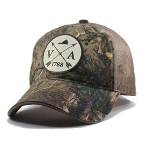 May include: A brown and green camouflage trucker hat with a white patch featuring a black outline of the state of Virginia, the letters "VA", two crossed arrows, and the year "1788".