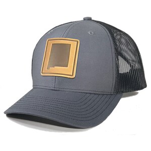 May include: A gray and black trucker hat with a brown leather patch featuring the outline of the state of New Mexico.