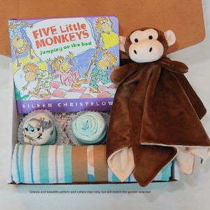 May include: A brown monkey plush toy with a white belly and a blue and green striped swaddle blanket. The monkey is holding a book titled "Five Little Monkeys Jumping on the Bed" by Eileen Christelow. There are two blue and white striped baby socks in the background.