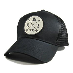 May include: Black trucker hat with a white patch featuring a crossed arrow design, the letters "RI", and the year "1790".