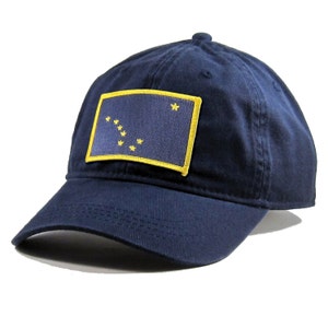 Peut inclure: Une casquette de baseball bleu marine avec un patch brodé jaune représentant le drapeau de l'État d'Alaska. Le drapeau a un fond bleu avec une étoile dorée et huit étoiles dorées en forme de la constellation de la Grande Ourse.