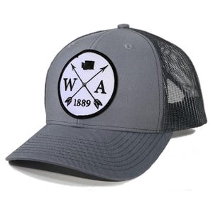 May include: Gray and black trucker hat with a white patch featuring a crossed arrow design and the text "WA 1889".