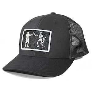 May include: Black trucker hat with a black mesh back. The front of the hat features a white embroidered patch of two skeletons toasting each other.