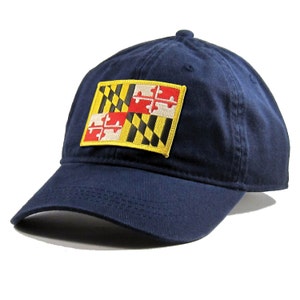 May include: A navy blue baseball cap with an embroidered patch of the Maryland state flag. The flag is yellow, black, and red with a white cross.