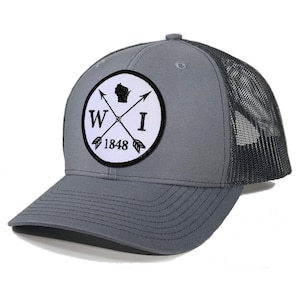 May include: A gray and black trucker hat with a white patch featuring the state of Wisconsin, the letters "WI", and the year "1848" in a circle with crossed arrows.