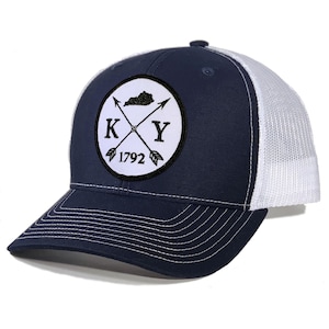 May include: A navy blue and white trucker hat with a white circle patch featuring a black outline of the state of Kentucky, crossed arrows, and the letters "KY" with the year "1792" below.