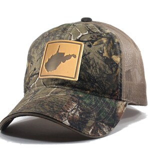 May include: A brown and green camouflage trucker hat with a brown leather patch featuring the outline of West Virginia. The hat has a mesh back.