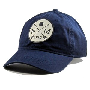 Peut inclure: Une casquette de baseball bleu marine avec un patch blanc représentant les lettres "NM" avec des flèches croisées et l'année "1912" en dessous.