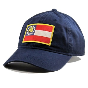 May include: A navy blue baseball cap with a yellow-trimmed patch featuring the Georgia state flag. The flag is red, white, and blue with a gold emblem in the top left corner.