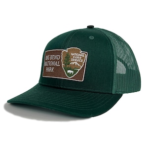 May include: A dark green trucker cap with a mesh back and a curved peak. The front has a rectangular patch with the text "BIG BEND NATIONAL PARK" and the National Park Service logo.