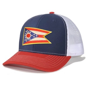 May include: A navy blue and red trucker hat with a white mesh back. The hat features a large embroidered patch of the Ohio state flag.