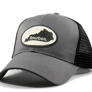 May include: Gray trucker hat with a black mesh back. The hat features a white oval patch with a black outline and the state of Kentucky with the word "Bourbon" printed in white.