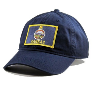 May include: A navy blue baseball cap with a yellow embroidered patch featuring the state flag of Kansas. The patch has the state seal and the word "KANSAS" in yellow.
