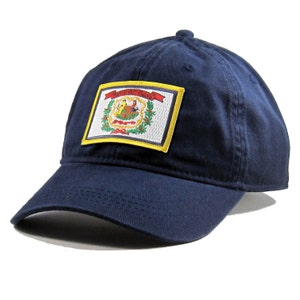 May include: A navy blue baseball cap with a patch featuring the state flag of West Virginia. The flag is white with a green wreath, a red bird, and a yellow ribbon with the words "Mountaine State" on it.