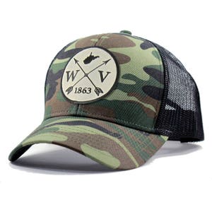 May include: A camouflage trucker hat with a black mesh back. The front of the hat features a white patch with a black outline of the state of West Virginia, two crossed arrows, and the letters "WV" and "1863".