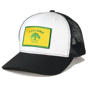 May include: White and black trucker hat with a green and yellow patch that says "Oakland 1832" with a green oak tree inside.