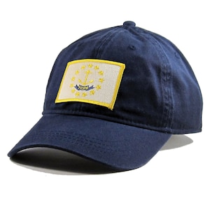May include: A navy blue baseball cap with a white and yellow embroidered patch of the state flag of Rhode Island. The patch features a white anchor with a yellow rope and the word "HOPE" in yellow.