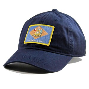 May include: A navy blue baseball cap with an embroidered patch of the Delaware state flag. The patch features the state seal and the text "December 7, 1787".