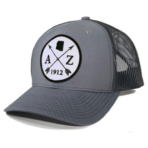 May include: A gray and black trucker hat with a white patch featuring a black outline of the state of Arizona, the letters "AZ" and the year "1912" with two crossed arrows.