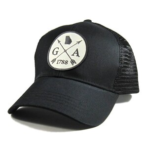 May include: Black trucker hat with a white patch featuring a crossed arrow design, the letters "GA", and the year "1788".