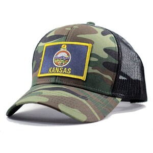 May include: A camouflage trucker hat with a black mesh back. The hat features a patch with the state flag of Kansas and the word "Kansas" in yellow lettering.