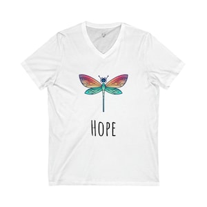 Puede incluir: Camiseta blanca de cuello en V con un gráfico de libélula colorido y la palabra "HOPE" impresa debajo.