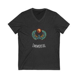 Puede incluir: Una camiseta de cuello en V gris oscuro con un gráfico de un escarabajo con alas y un sol detrás. El texto "IMMORTAL" está impreso debajo del gráfico.