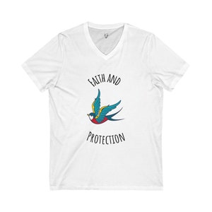 Puede incluir: Camiseta blanca de cuello en V con un gráfico de golondrina azul y amarilla y el texto "Faith and Protection" impreso en negro.