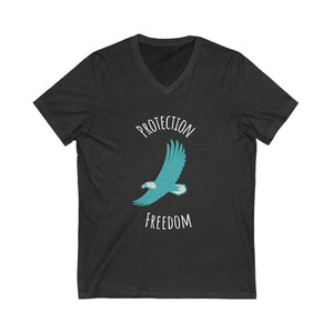 Puede incluir: Una camiseta de cuello en V gris oscuro con un águila azul turquesa volando con el texto "PROTECTION FREEDOM" en blanco.