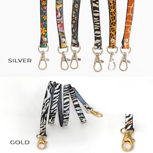 K&ouml;nnte beinhalten: F&uuml;nf bunte gemusterte Lanyards mit silbernen Drehverschl&uuml;ssen. Die Lanyards sind mit ge&ouml;ffneten Verschl&uuml;ssen dargestellt. Das Wort "SILVER" ist unter den Lanyards gedruckt. Drei der gleichen Lanyards sind in einem Stapel mit einem goldenen Drehverschluss dargestellt. Das Wort "GOLD" ist unter den Lanyards gedruckt.