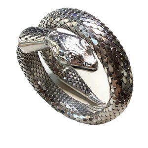 Könnte beinhalten: Ein silberfarbenes Schlangenarmband in einer spiralförmigen Form. Der Schlangenkopf ist detailliert mit Schuppen und einer spitzen Zunge. Das Armband besteht aus kleinen, reflektierenden Metallstücken.