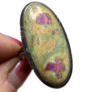 Könnte beinhalten: Ein silberner Ring mit einem ovalen, grün-rosa Edelstein. Der Edelstein hat ein gesprenkeltes Muster und ist in einer silbernen Fassung gefasst.