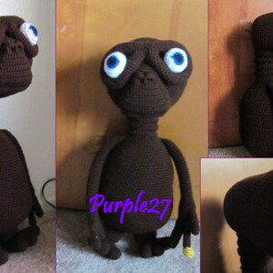 Pode incluir: Um brinquedo de pelúcia de crochê marrom que se assemelha ao personagem alienígena E.T. O brinquedo tem olhos grandes e brancos com pupilas azuis e um pescoço comprido. O brinquedo está em pé em um chão de madeira.
