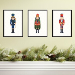May include: Three framed watercolor paintings of nutcracker soldiers. The nutcrackers are wearing traditional costumes with red, blue, and green accents. The frames are black and the background is a light green wall.