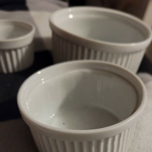 May include: Three white ceramic ramekins of different sizes. The ramekins have a fluted design and are perfect for baking individual desserts.