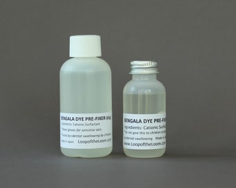 May include: Two clear plastic bottles with white labels. The bottles contain a clear liquid and are labeled "Bengala Dye Pre-Fixer (65g)". The label includes instructions to wear gloves for sensitive skin and to avoid accidental swallowing by children. The bottles are made in Japan and are sold by LoopoftheLoom.com.