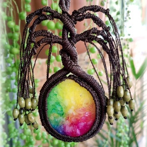 May include: A rainbow agate crystal is encased in a brown macrame tree of life pendant. The pendant has a beaded fringe.