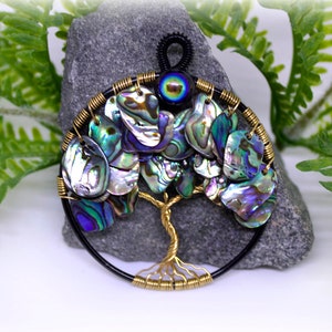 May include: A wire wrapped tree of life pendant featuring iridescent abalone shell leaves and a black and blue evil eye charm.