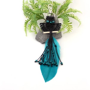 Puede incluir: Llavero de búho de macramé negro con pluma azul turquesa y cuentas.