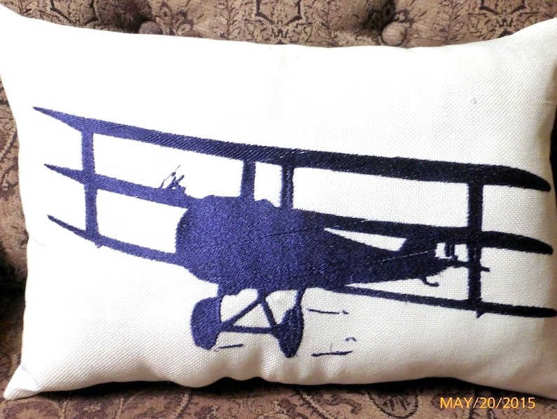A white rectangle pillow with a Navy blue embroidered antique Bi-Plane across the front.